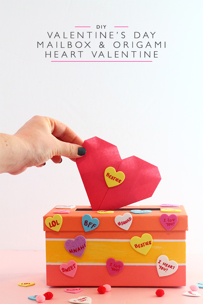 Hand putting a pink origami heart into a colorful valentine's day mailbox covered in conversation heart stickers. Written on the image is DIY Valentine's Day Mailbox and Origami Heart Valentine